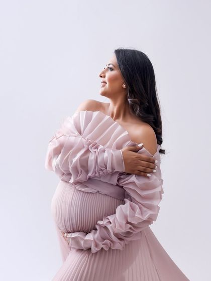 A portrait of graceful elegance. The soft pink pleated gown and the mom-to-be's serene expression create a beautiful and timeless image.