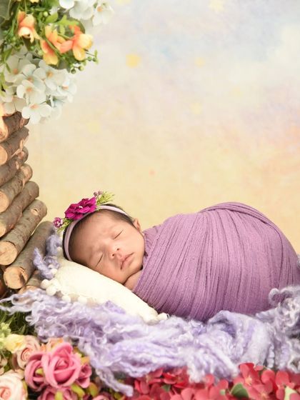 A close-up of a baby in a purple wrap, nestled in a floral basket. The soft colors and textures create a gentle and beautiful portrait.