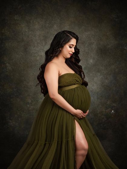 A classic and graceful profile shot in an olive green tulle gown. The simple, dark background and soft lighting create an elegant and timeless maternity portrait.