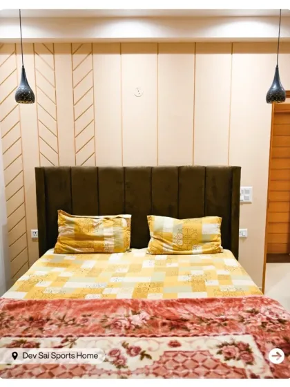 This bedroom features a high upholstered headboard and a geometric-paneled accent wall. The hanging pendant lights serve as stylish alternatives to bedside lamps.