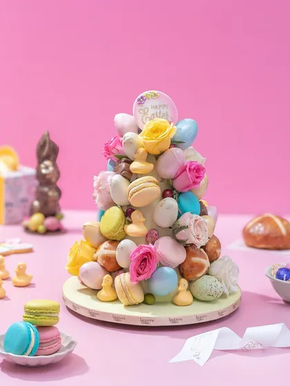 Our Easter Treat Tower, a playful and colourful centerpiece made of macarons, hot cross bun bites, and mini chocolate eggs, all adorned with fresh roses.