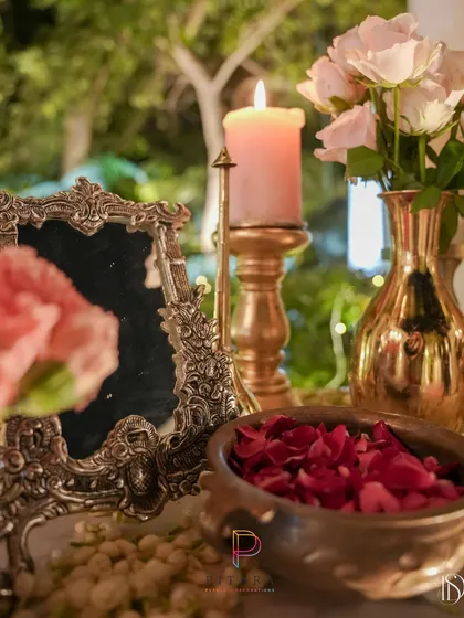 A romantic vignette with a vintage silver-plated picture frame, a bowl of red rose petals, and a thick pink candle in a brass holder. These details create a warm and timeless feel.