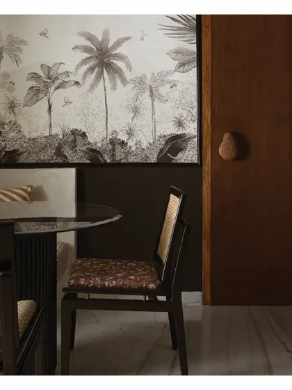 We created a cozy dining nook in this home by pairing a built-in bench with a tropical black-and-white artwork. The custom seating makes excellent use of a corner, while the bespoke wood door handle offers a tactile, welcoming touch upon entry.