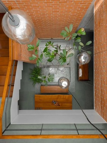 A top-down view into the central courtyard highlights how this small pocket of green is a source of light and life for the surrounding spaces. The hanging pendant lights add a touch of industrial elegance to the rustic brick and plant life.