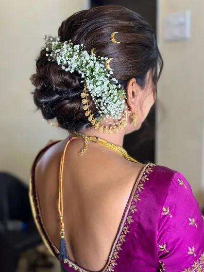A traditional bridal bun adorned with baby's breath and a classic jhumka-style hair accessory.