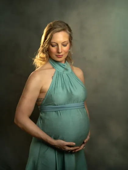 A contemplative pose from a studio maternity session. The expecting mother looks down at her belly, her hands cradling it gently, against a painterly, textured backdrop.