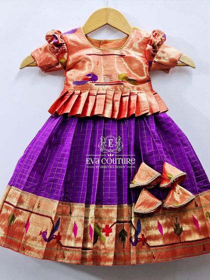 A pure Paithani handloom silk lehenga for toddlers. The peach blouse has a pleated peplum, and the purple skirt has a traditional Paithani border.