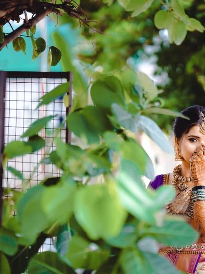 A playful and candid shot where the bride peeks through lush green leaves. This style of photography helps our clients relax and be themselves, resulting in natural and charming portraits that reveal their personality.
