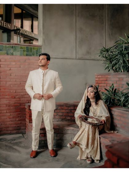 A beautifully composed shot of the couple, with the bride seated and holding a mirror, and the groom standing, creating a scene of classic elegance.