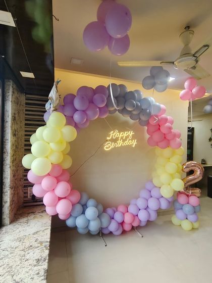 A beautiful pastel rainbow theme for a 2nd birthday party at home. The large circular balloon arch creates a stunning backdrop, complemented by a neon sign and a balloon number '2'.