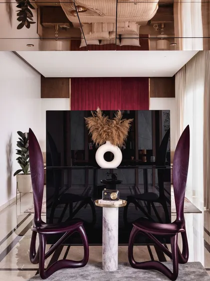 The home office area is separated from the bedroom by a monolithic TV unit that acts as a dynamic partition. The sculptural purple chairs add a pop of color and artistic flair to this private workspace.