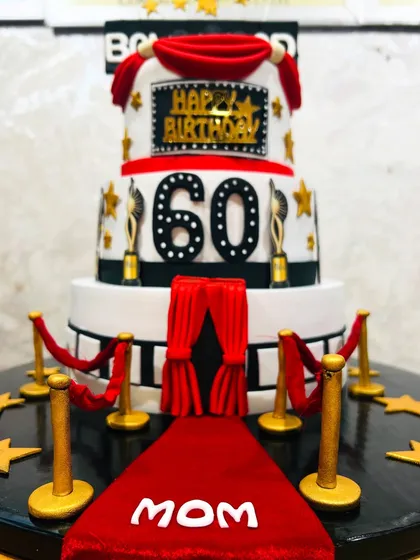 A close-up of the spectacular three-tier Bollywood-themed cake for a 60th birthday, showing the red carpet and velvet ropes.