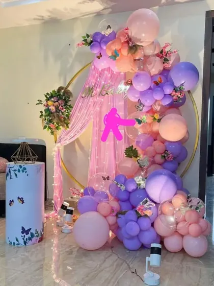 A whimsical butterfly and fairy theme with a circular gold frame. The decoration features a pink curtain, a balloon garland, and a butterfly-themed pedestal.