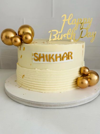A simple and elegant white and gold birthday cake with textured buttercream and golden spheres.