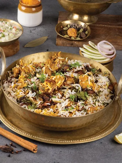A large handi of chicken biryani, styled with traditional Indian spices and raita. The composition is rich and abundant, perfect for a family-style restaurant.