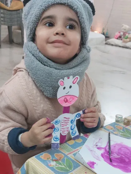 A close-up of a smiling child with her handmade puppet. Creating puppets encourages storytelling and imaginative play long after the art session is over.