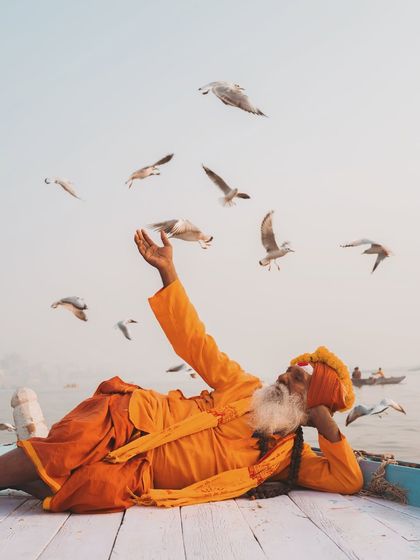 A sadhu lies back on a boat, feeding the seagulls that flock over the Ganga. It's a moment of pure, unscripted joy and connection with nature in the heart of the holy city.