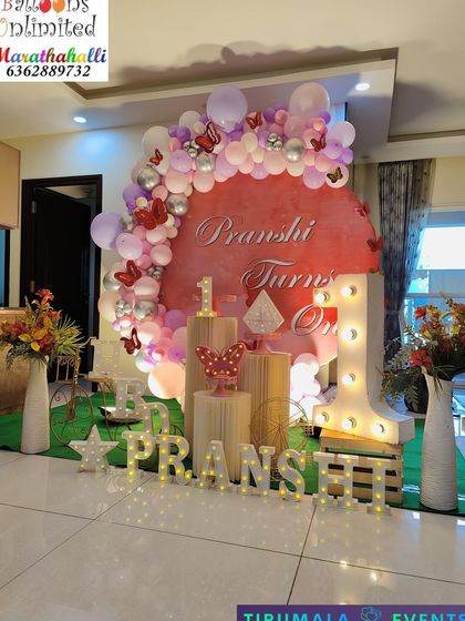 A lovely butterfly theme for a first birthday, designed with a circular backdrop, marquee lights for the name, and elegant wooden plinths.