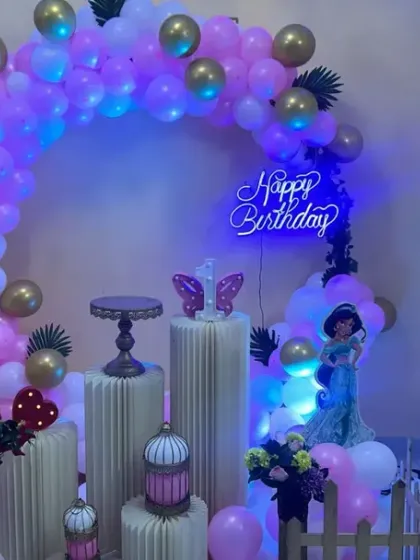 This princess theme uses blue backlighting to create a cool, magical glow. The pink and gold balloon arch with Jasmine and Aurora cutouts looks stunning against the light.