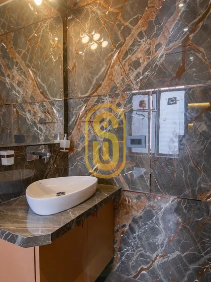Another view of the dark marble bathroom, focusing on the vanity area. The uniquely shaped mirror and countertop sink add a touch of artistic flair to the functional space.