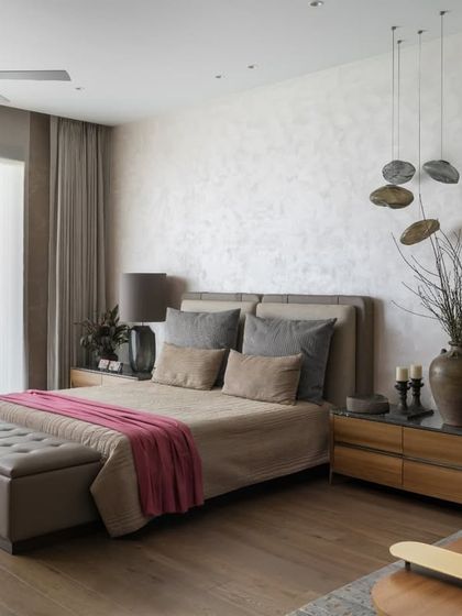 The sleeping area of the master bedroom is a study in serene luxury. A textured wall finish, cascading pendant lights, and a palette of soft greys and pinks create a calm and inviting atmosphere, perfect for rest and rejuvenation.