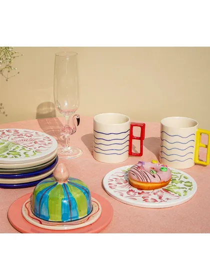 A playful and colorful collection of handmade ceramic tableware, including mugs and a butter dish, styled with a donut.