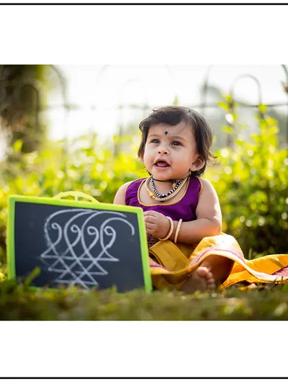A sweet outdoor portrait of a baby girl in a traditional outfit, sitting in the grass with a small chalkboard prop. I can incorporate meaningful items into your session.