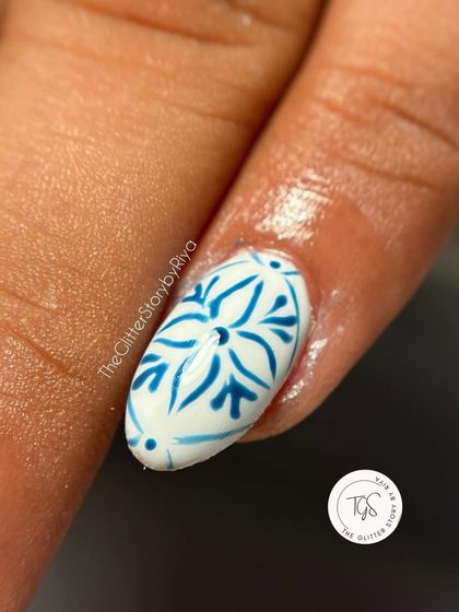 A macro shot of a nail with a beautifully intricate, hand-painted blue and white pattern inspired by Mediterranean tiles.