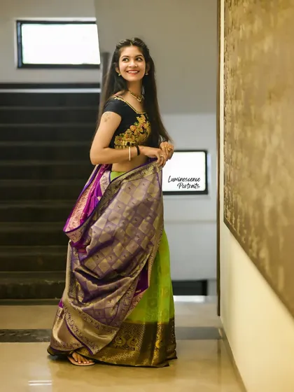 A full-length shot of a stunning half-saree, showcasing the contrast between the green skirt and purple dupatta in a modern indoor setting.
