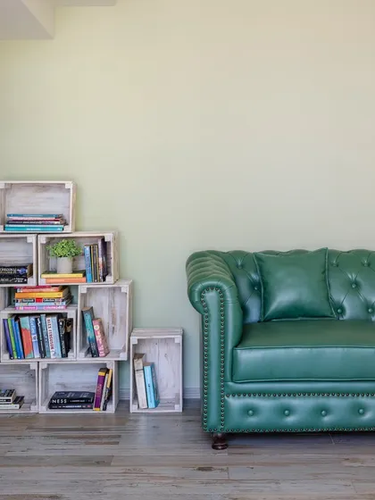 A quiet reading corner featuring a classic green leather Chesterfield sofa and a modular bookshelf made from distressed wooden crates. This space combines timeless design with a relaxed, rustic vibe.