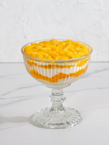 A single serving of our Mango Cream Cheese Trifle in a beautiful glass goblet, highlighting the vibrant layers of white cream and yellow mango.