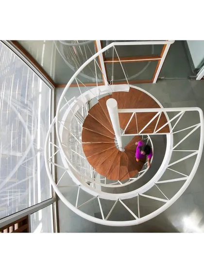 The spiral staircase is a key elemental feature connecting the main studio with the public interaction space above. This top-down view reveals its "woven" steel structure and recycled teak wood treads, forming a perfect, sculptural spiral.