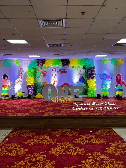 A large-scale jungle theme decoration on a banquet hall stage. The setup includes a balloon arch, animal cutouts, and 'ONE' table letters for a first birthday.