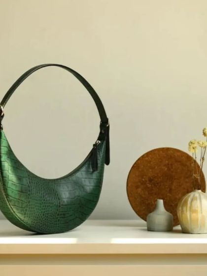 A still life of the Selena in Forest Green. This shot highlights the bag's perfect crescent shape and the subtle texture of its croc-embossed leather.