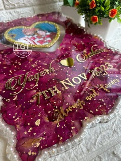 An angled view showing the golden text with the couple's names and wedding date over a bed of preserved red rose petals.