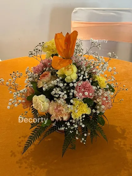 A colorful floral centerpiece for a traditional event, using a mix of carnations and tulips that complement the orange table linen.