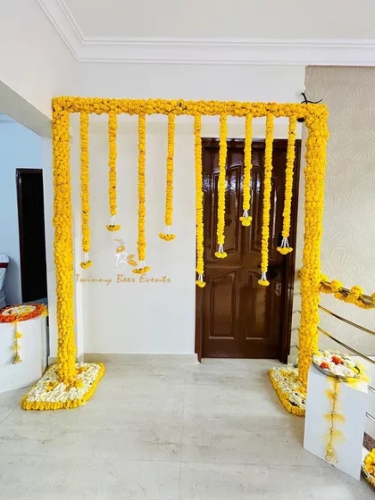 A classic and vibrant Haldi ceremony backdrop. This simple yet elegant design features a frame fully covered in bright yellow marigolds with hanging floral strings, perfect for home-based pre-wedding functions.