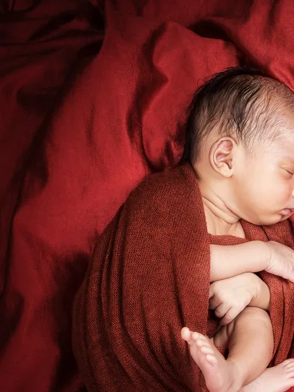 A dramatic and moody portrait using a deep red wrap and background. This style creates a rich, artistic feel, focusing on the baby's curled-up form.