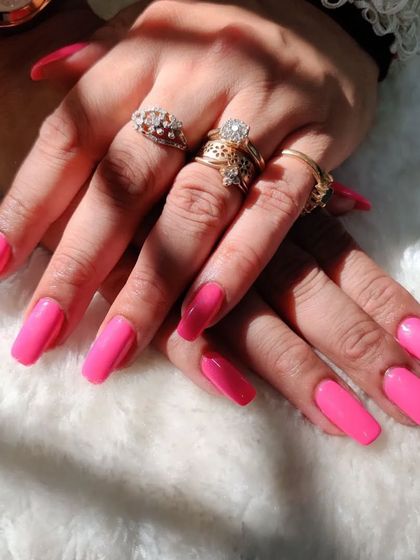 A full view of the stunning, vibrant pink nails, beautifully accessorized with the client's rings.