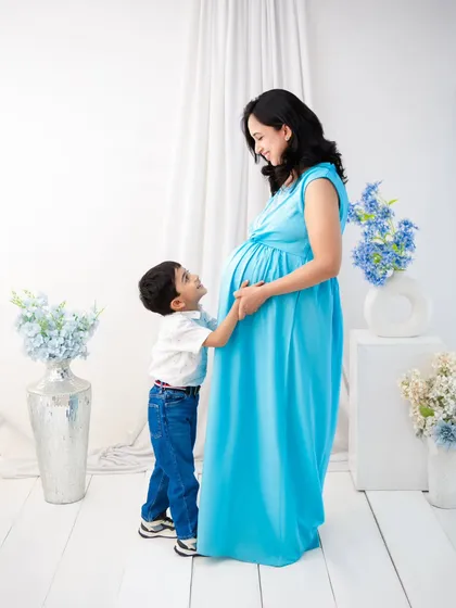 A son's gentle touch on his mother's baby bump. Set against a clean, minimalist backdrop with hints of blue, this image is a testament to the growing bond.