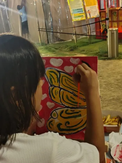 A young artist concentrates on adding the finishing touches to her butterfly painting during an outdoor craft session.