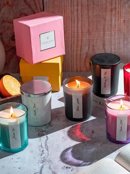 Our scented candles are perfect for creating ambiance and cozy moments. This arrangement shows our colorful glass candles alongside fresh oranges and books, illustrating how they fit into your daily life.