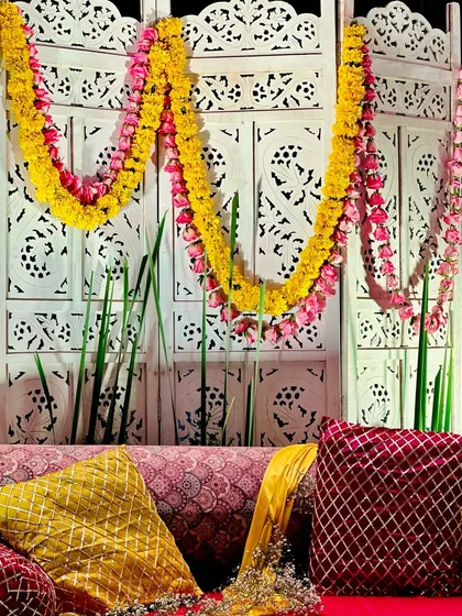 A view of the Mehendi seating, focusing on the white carved backdrop decorated with pink and yellow flower garlands.