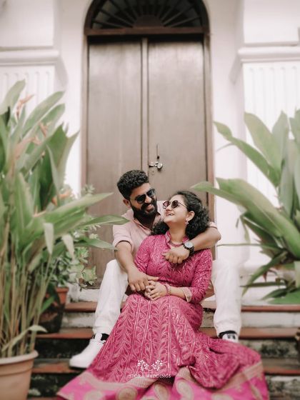 The couple seated on steps, surrounded by plants, sharing a relaxed and intimate moment.