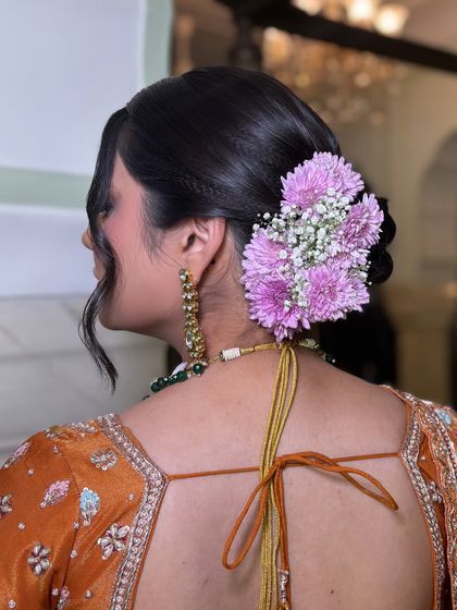 A side profile of the floral braided bun, showing how the flowers are placed to complement the client's features. This is a perfect example of a soft and elegant hairstyle for a wedding guest or bridesmaid.