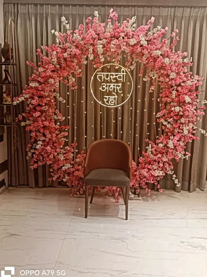 A circular arch made entirely of pink cherry blossoms for a Jain ceremony. This setup provides a delicate and beautiful frame for the main seat, complemented by a neon "Tapasvi Amar Raho" sign.