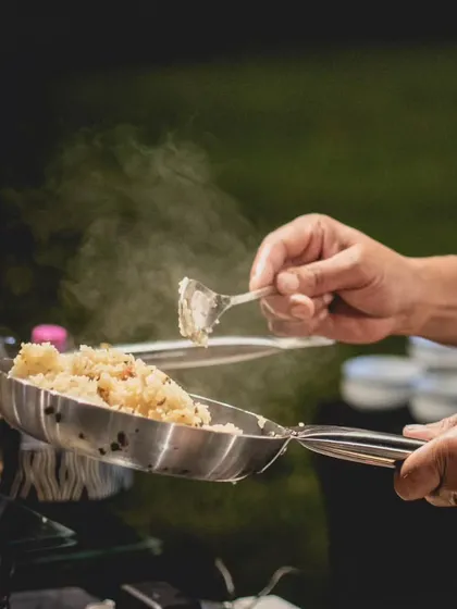 A chef serves up a freshly tossed dish from a steaming pan at an outdoor event. Our live stations are designed to handle any setting, ensuring your guests enjoy hot, gourmet food made to order.