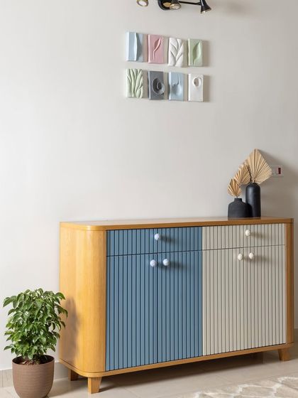 This custom fluted crockery unit, painted in pastel blue and ivory, adds elegant charm to the dining space. Above it, custom ceramic artwork ties together the home's overall pastel theme.