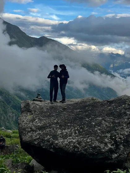 A couple standing on a large boulder on the Yulla Kanda trek, with clouds rolling through the valley below.