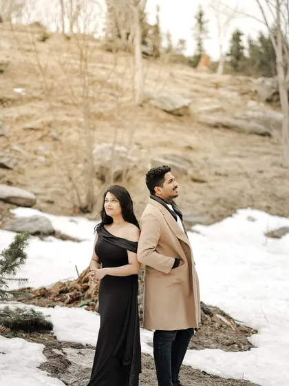 A stylish pose of a couple standing back-to-back against a snowy, barren landscape in Manali.